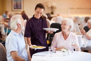 A female chef serving a couple of seniors in a community
